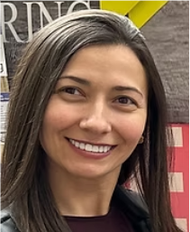 Smiling woman with shoulder-length gray hair in front of a bookshelf, wearing a dark jacket.