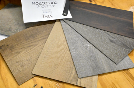 Assorted wood and gray flooring sample planks fanned out on a table with a small product label.