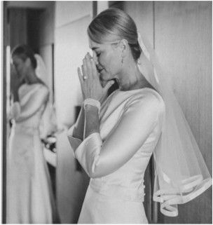 A woman in a wedding dress is praying in front of a mirror.