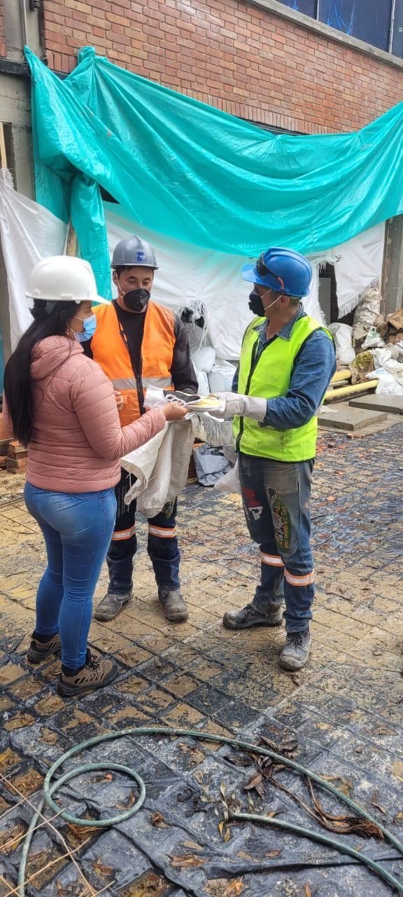 Tres trabajadores con cascos y chalecos de seguridad revisan los planos en una obra de construcción.