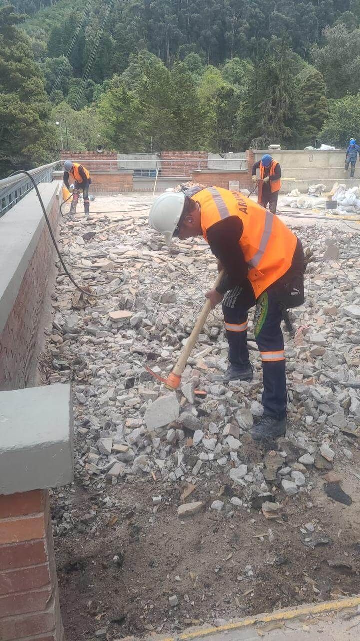 Trabajadores con chalecos de seguridad naranjas paleando grava en una obra de construcción con bloques de hormigón cerca.