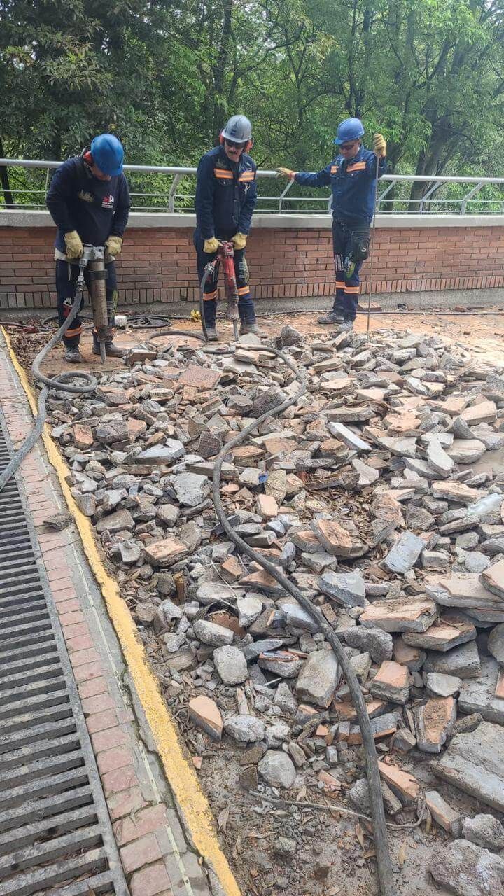 Tres trabajadores con cascos azules están rompiendo el pavimento viejo en un sendero bordeado de ladrillos.