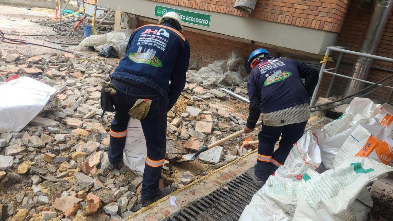 Dos trabajadores con cascos retiran escombros en la entrada de un edificio dañado.