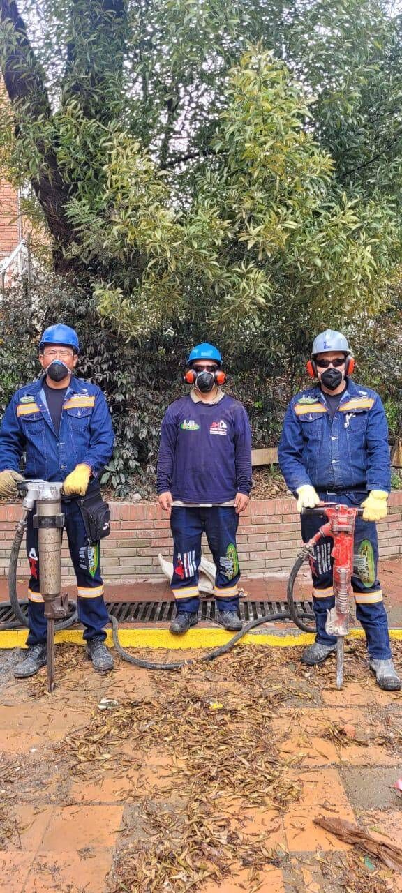 Tres trabajadores con uniformes azules y cascos permanecen de pie