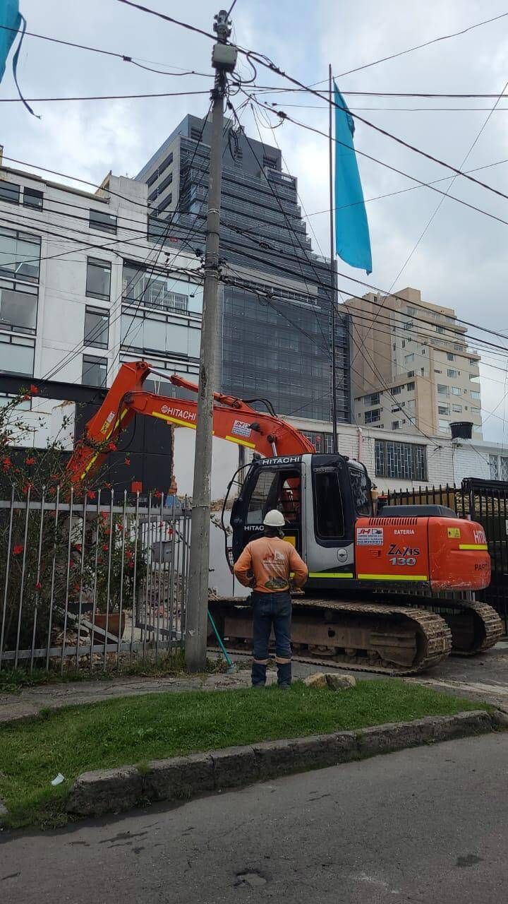 Una excavadora naranja se encuentra junto a una obra vallada
