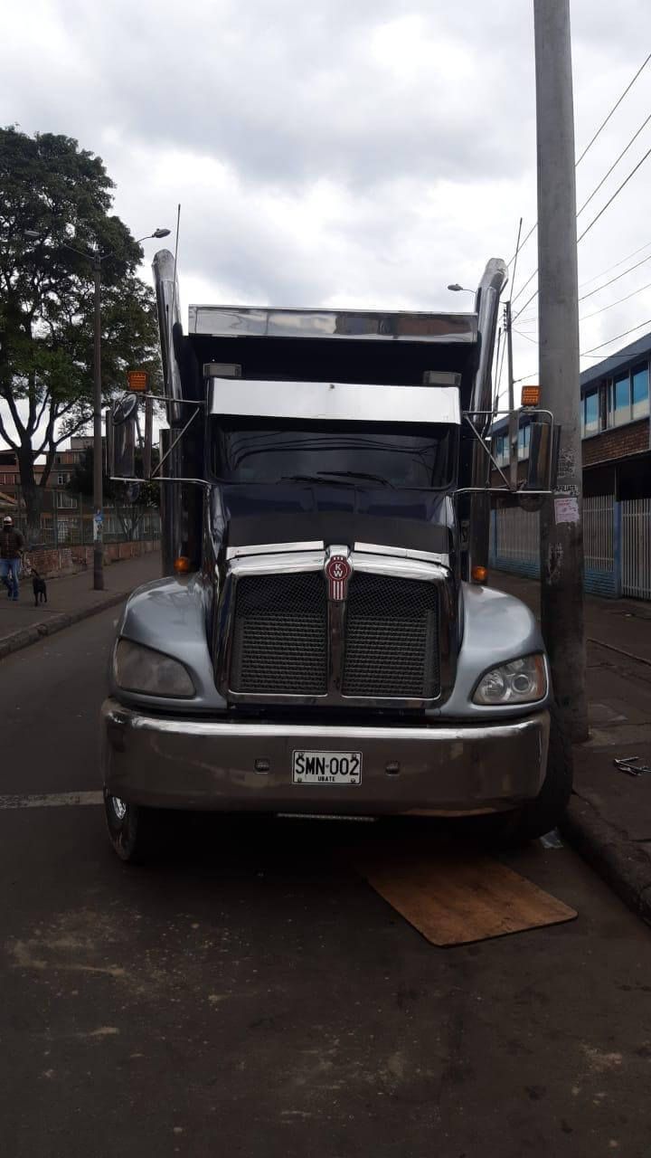 Vista frontal de un camión semirremolque gris estacionado en una calle bajo un cielo nublado.