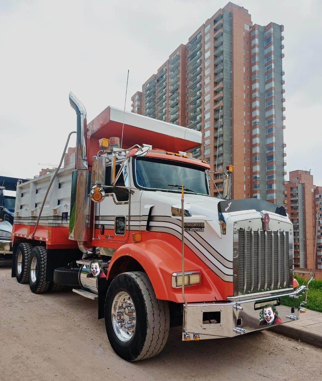 Un camión volquete rojo y blanco estacionado frente a un alto edificio de apartamentos.