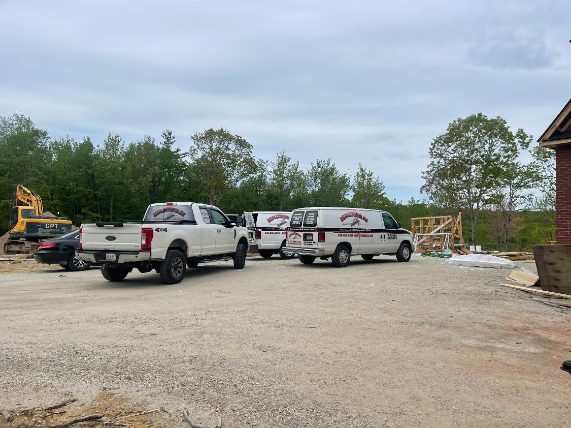 A group of white trucks and vans are parked in a gravel lot.