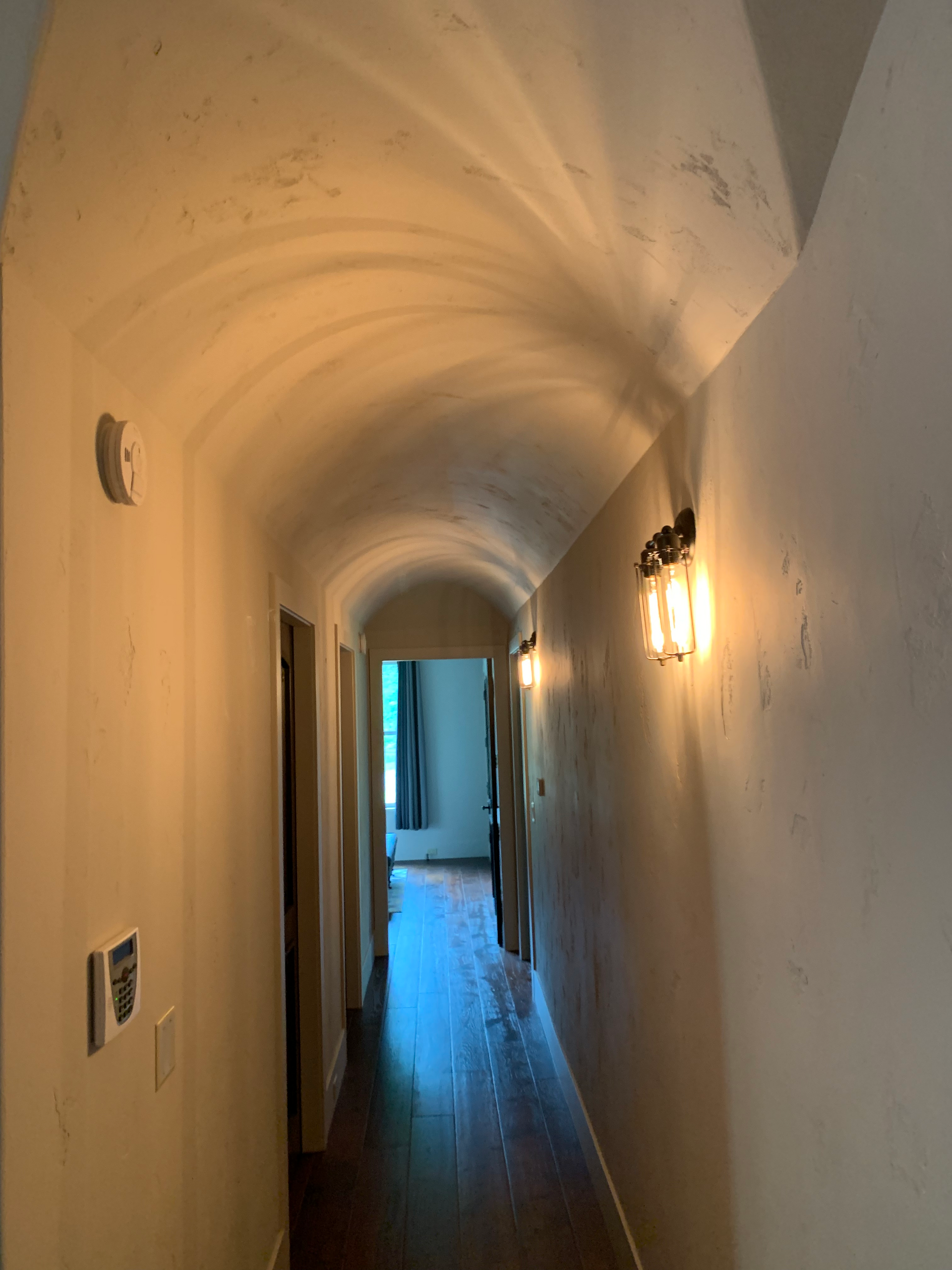 A long hallway with a vaulted ceiling and a light on the wall.