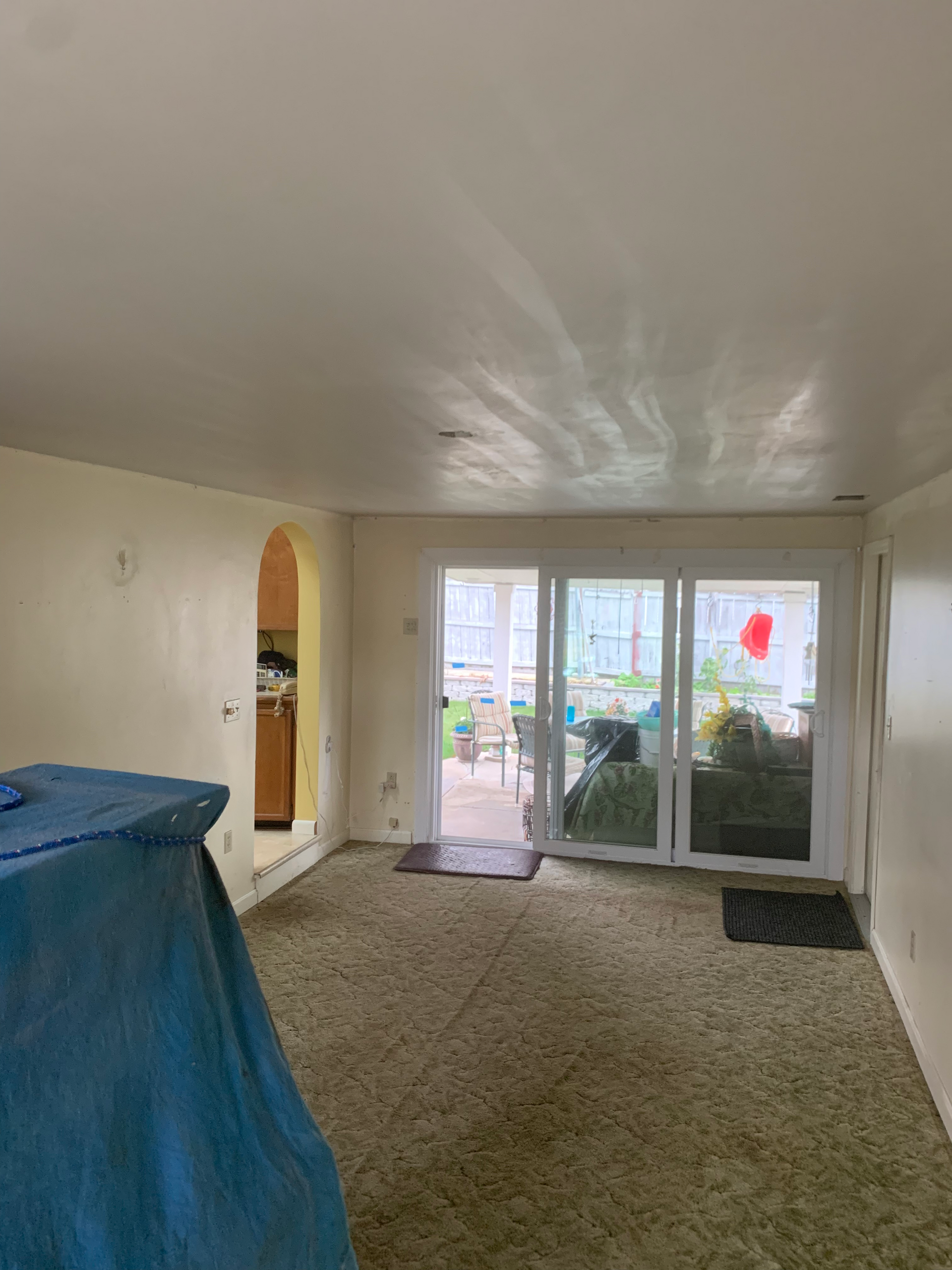 An empty living room with sliding glass doors and a blue tarp on the floor.