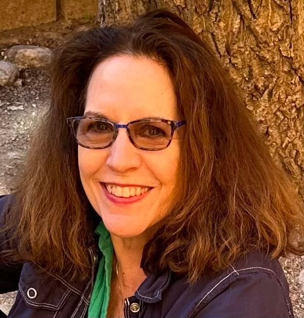 Woman with brown hair and glasses smiles outside.