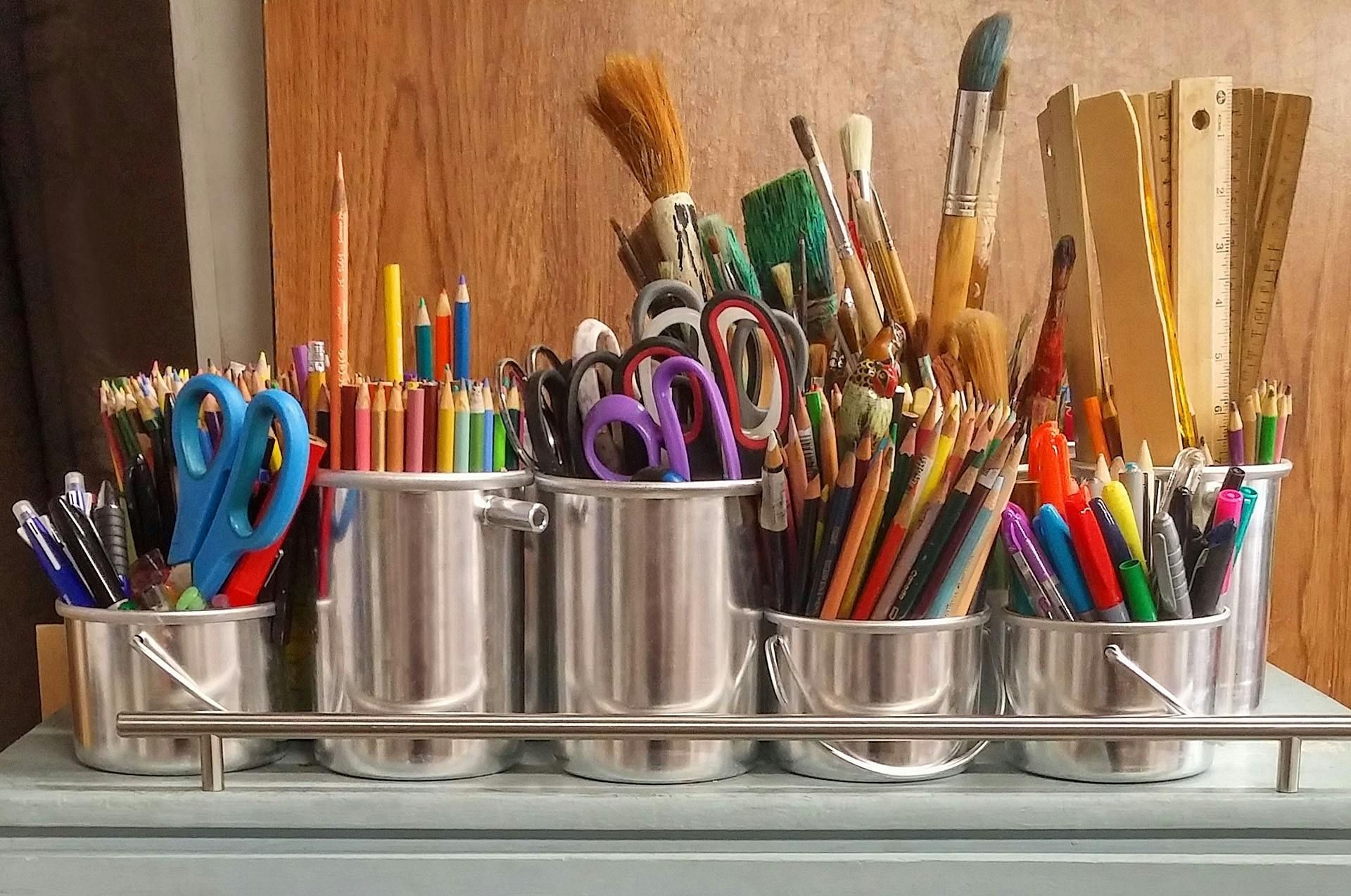 Art supplies organized in metal buckets: pencils, scissors, brushes, rulers, and pens.
