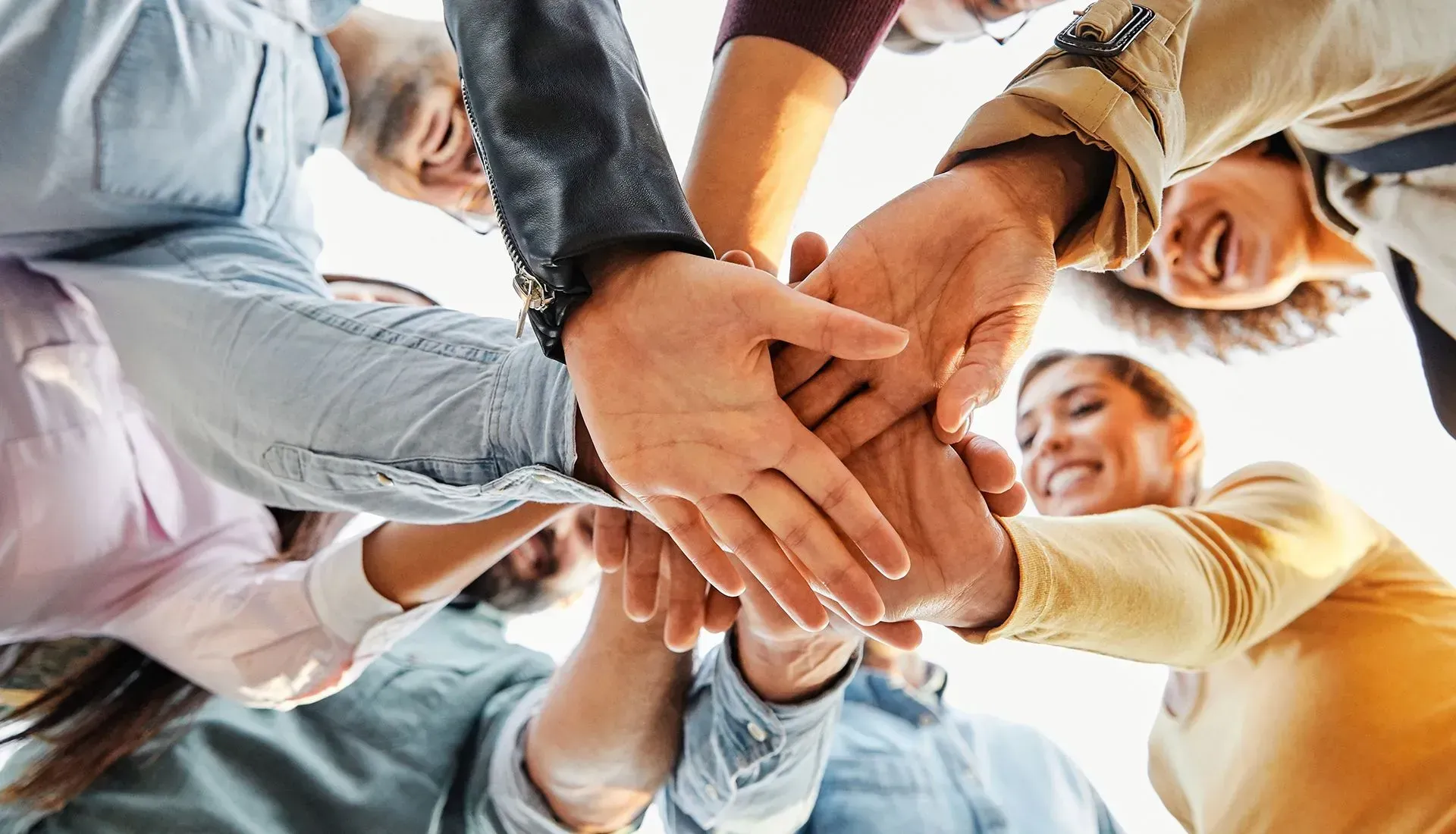 People with hands joined together in a circle, viewed from below, smiling.