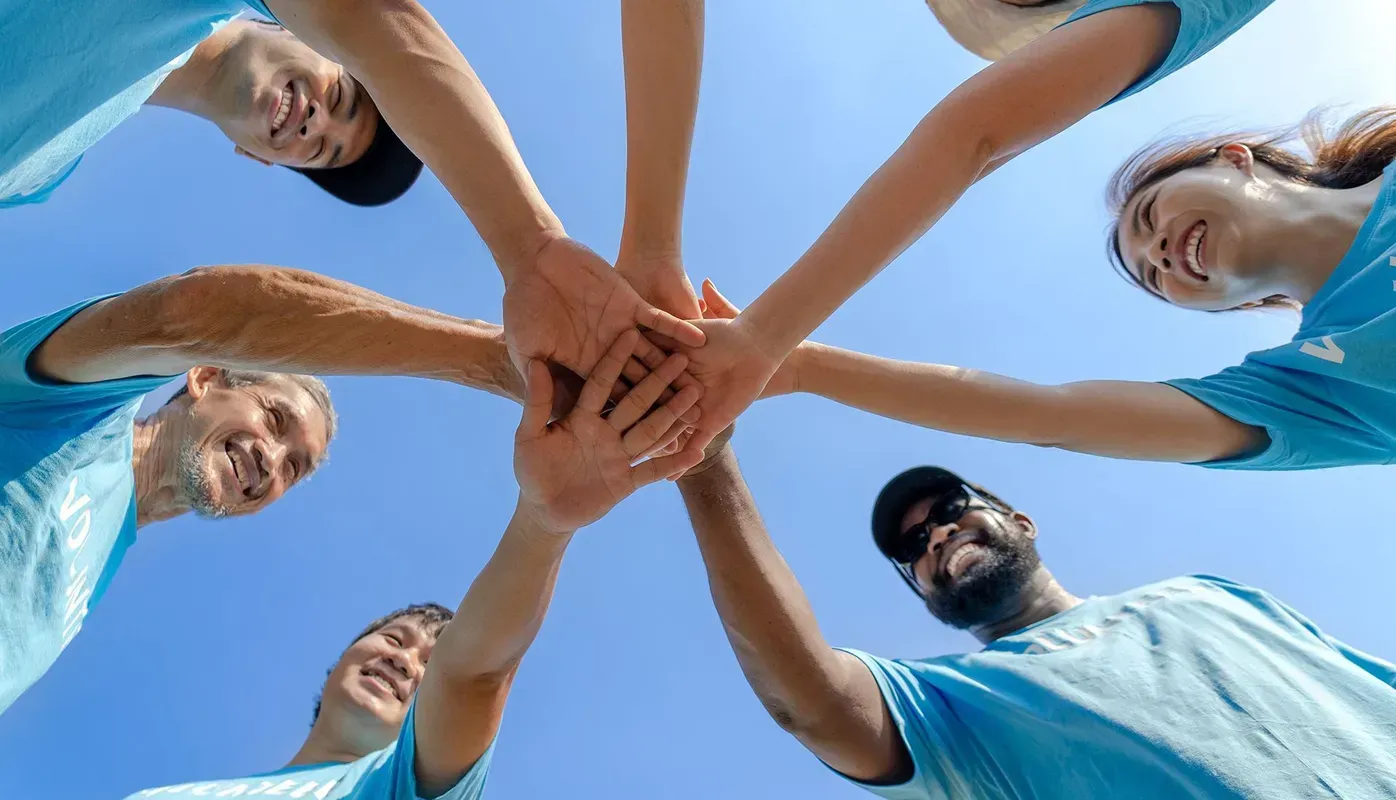 Group of people with hands together in a circle, blue sky background.