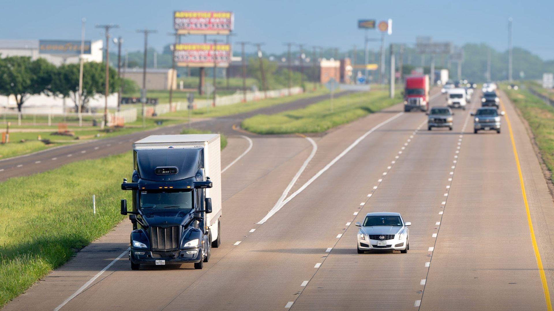 A semi truck is driving down a Dallas TX highway next to a car.