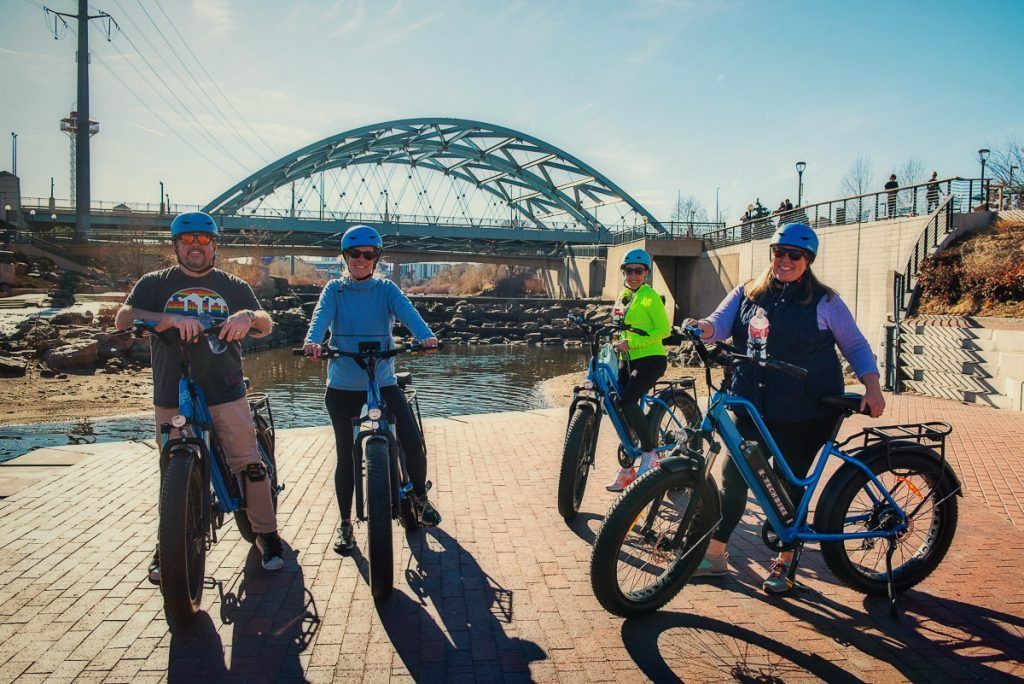 A group of people are standing next to each other on bicycles in front of a bridge in BOLDER CO
