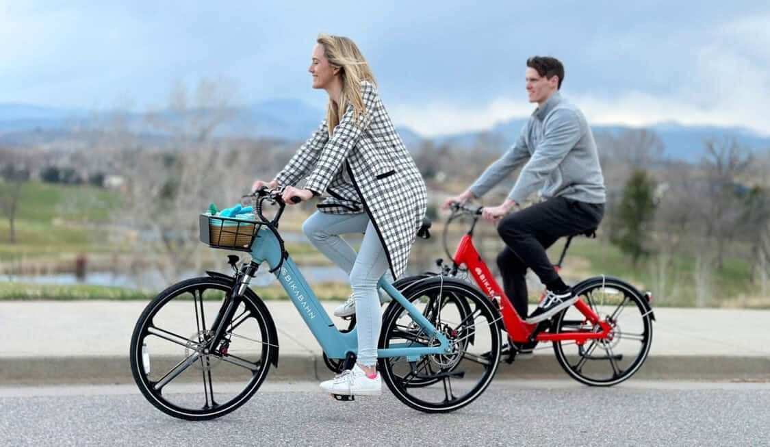 A man and a woman are riding bicycles down a street in bolder CO