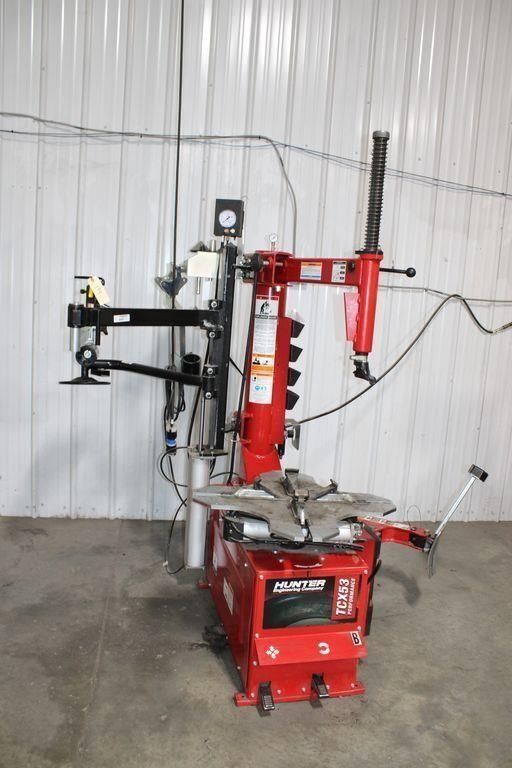 Red tire-changing machine in a garage against a white corrugated wall.