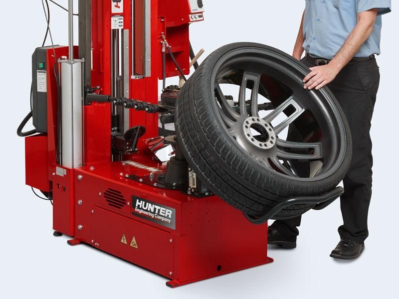 Red tire-changing machine lifting a car wheel beside a standing mechanic