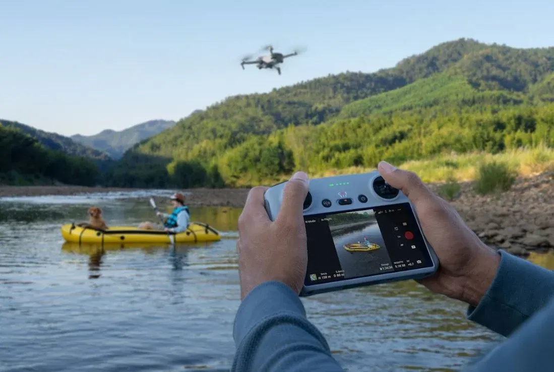 A person is holding a DJI mini 3 drone remote control over a kayak in the water.