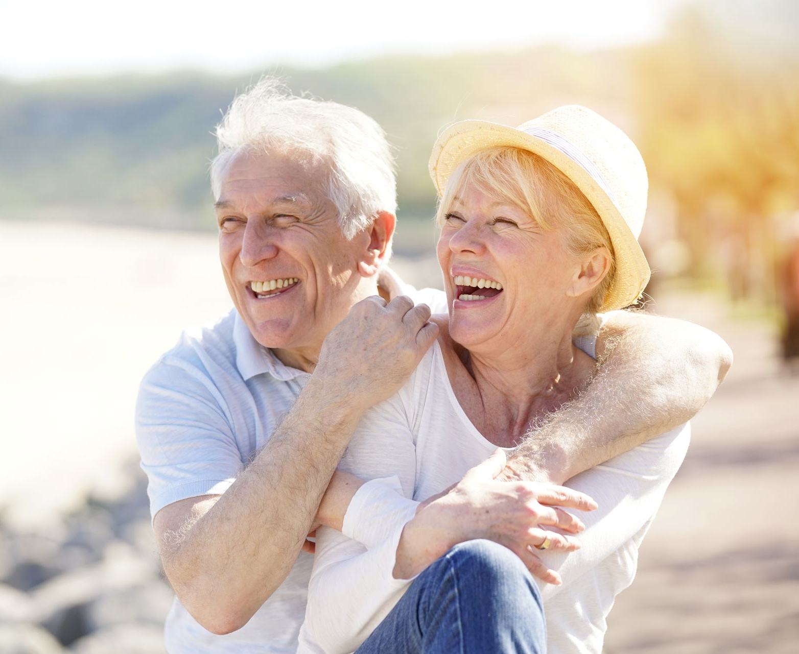 Smiling couple embracing outdoors; woman wearing a hat; sunny background.