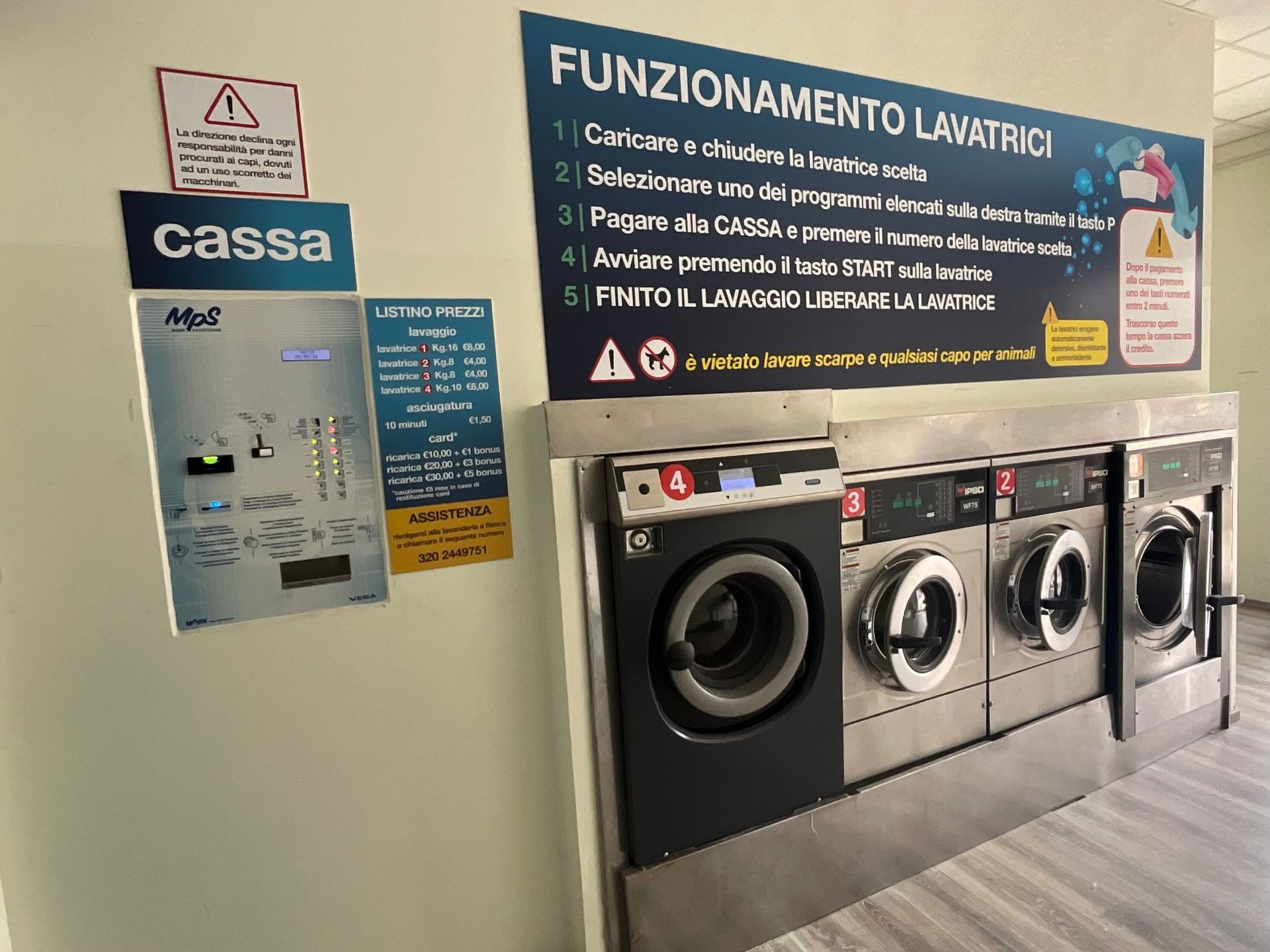 Lavanderia con quattro lavatrici a carica frontale e cartelli con le istruzioni in italiano sulla parete.