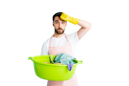 Un uomo dall'aria stanca, con un guanto giallo in testa, che regge un cesto della biancheria verde brillante, stagliarsi su uno sfondo bianco.