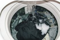 Lavatrice a carica dall'alto piena di vestiti bagnati e acqua saponata che si riversa dentro