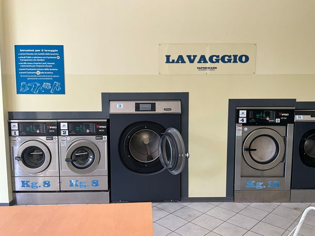 In una lavanderia a gettoni ci sono sei asciugatrici a carica frontale, una delle quali piena di vestiti bianchi.