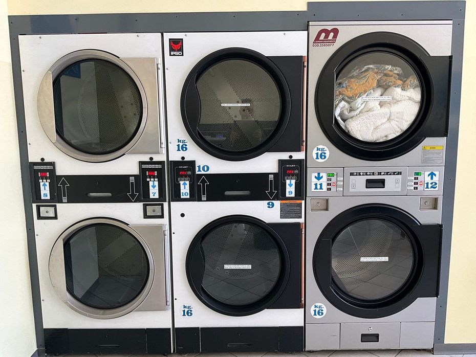 Una donna carica la biancheria in una lavatrice industriale, tenendo in mano un cesto in una lavanderia.