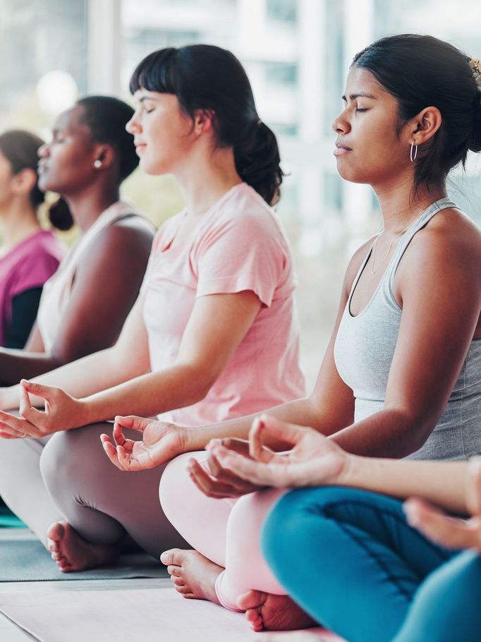 a group of women sit on yoga mats with their eyes closed