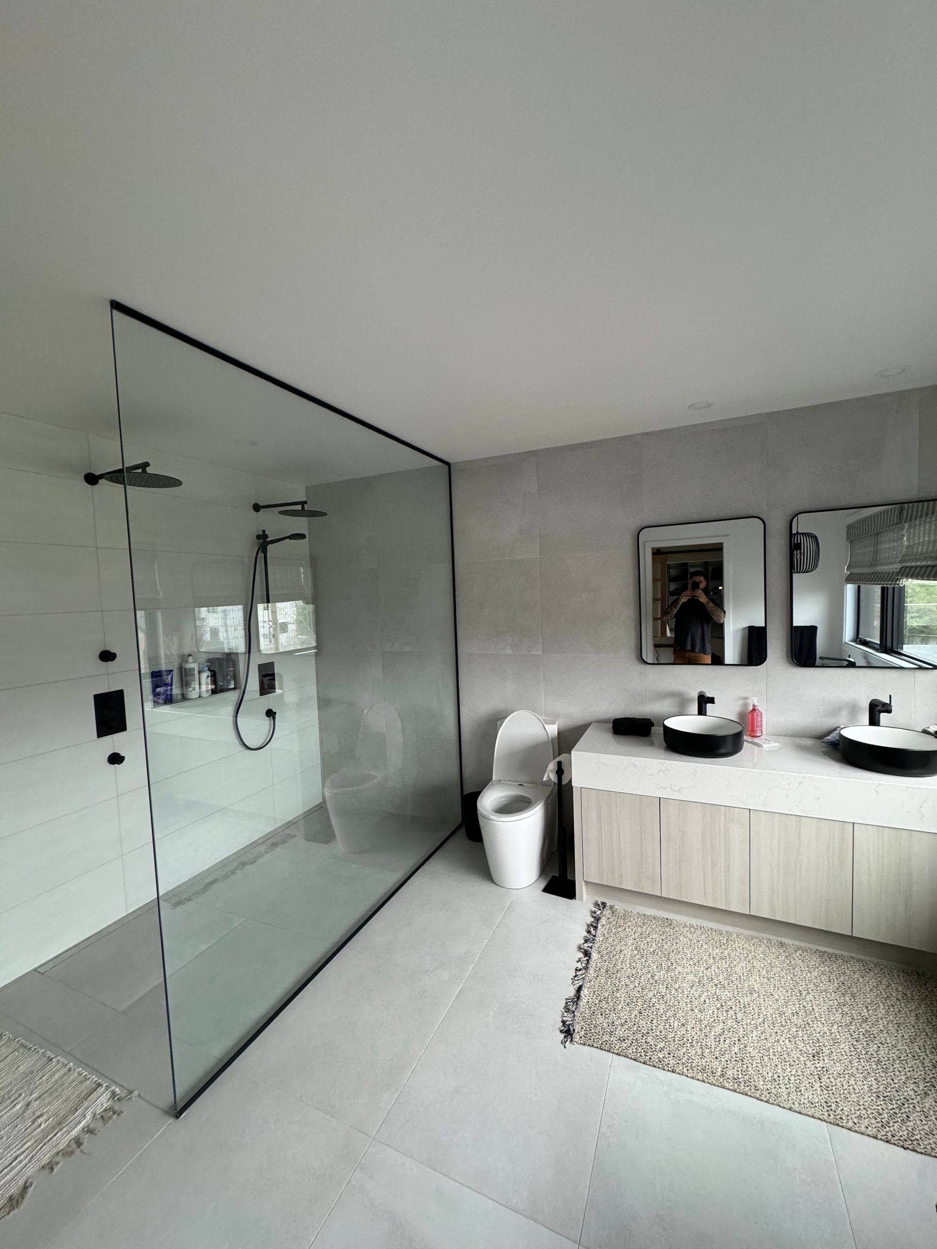 Salle de bains moderne avec douche en verre, double vasque et sol beige.