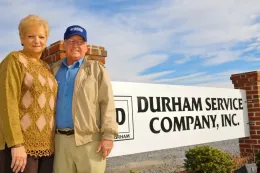 Two people standing by a Durham Service Company, Inc. sign under a blue sky