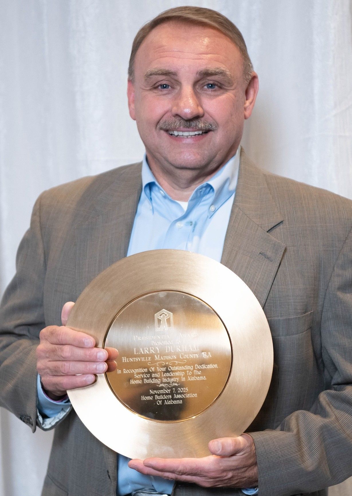Man holding a large gold award plaque and smiling in front of a white curtain