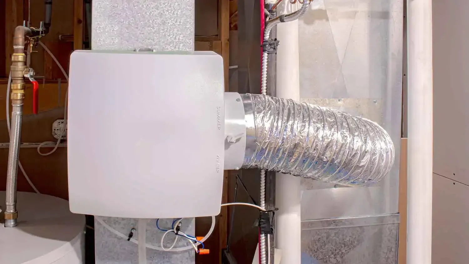 White HVAC ducting and insulated ventilation hose in a utility room with pipes and equipment.