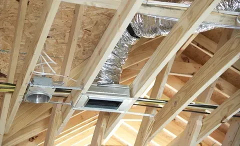 Exposed attic framing with metal HVAC ducts and vents running through wooden rafters