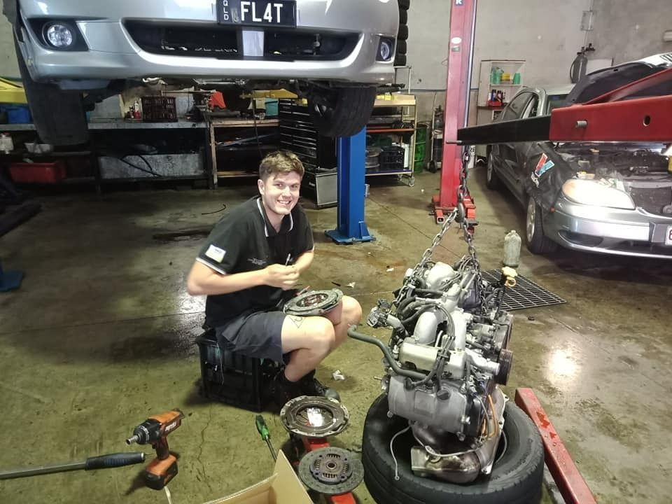 A Man Is Kneeling Next To A Car Engine With A License Plate That Says Flat — Marcoola Tyre & Mechanical In Marcoola, QLD