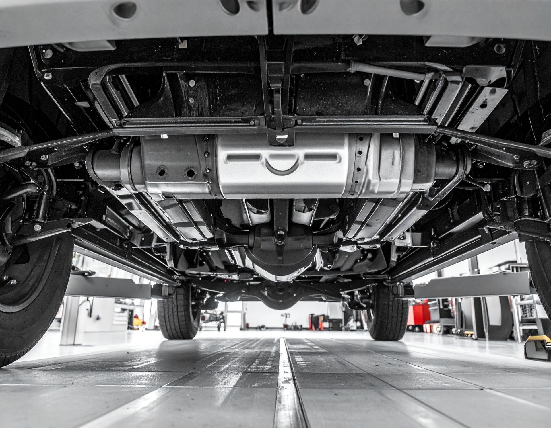 Underbody view of a vehicle on a lift, showing the chassis and exhaust system in a garage