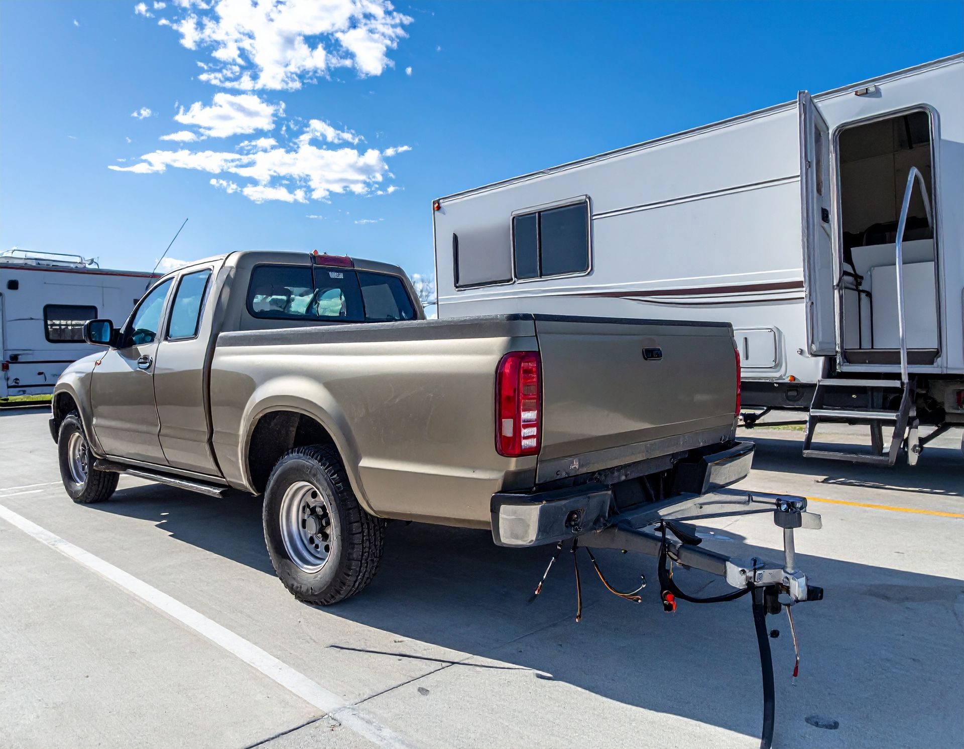 Tan pickup truck towing a white camper trailer in a parking lot under a blue sky
