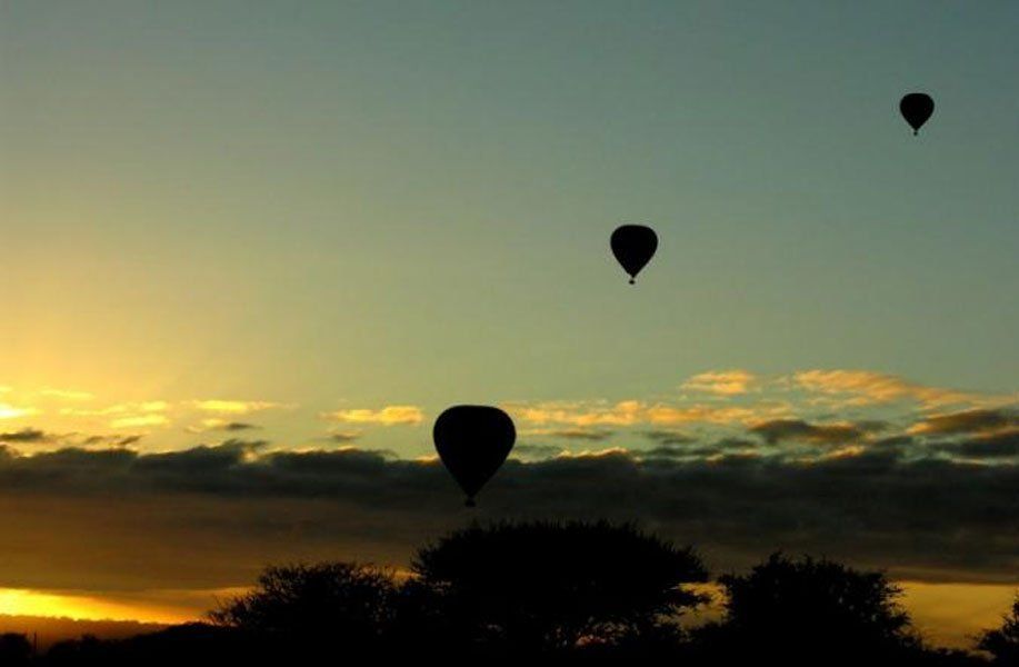 Three hot air balloons are flying in the sky at sunset.