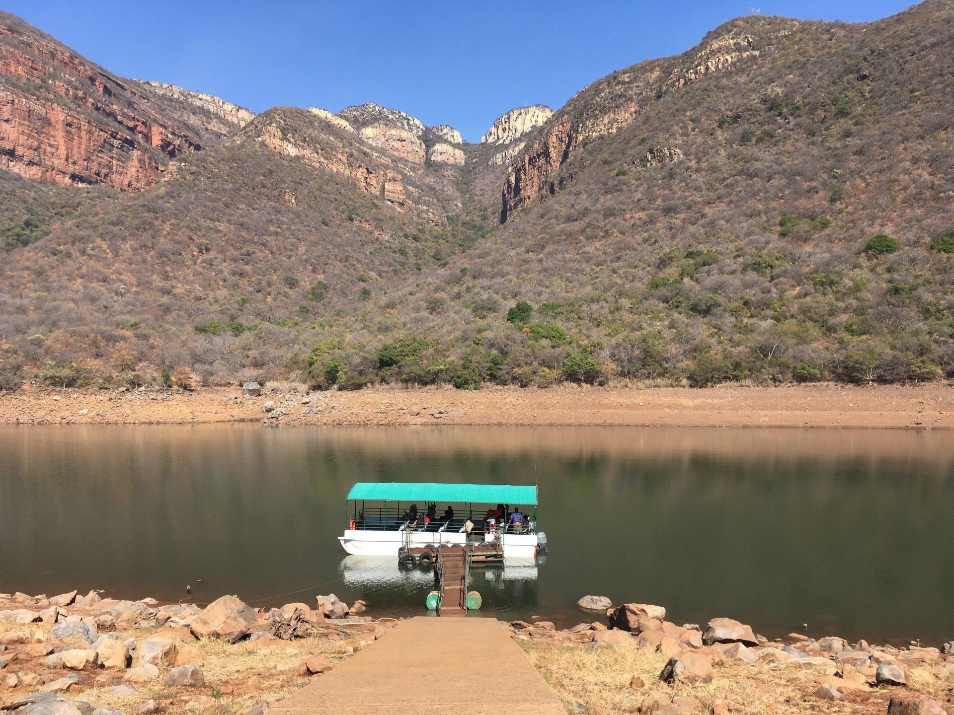 A boat with a green roof is floating on a lake with mountains in the background.
