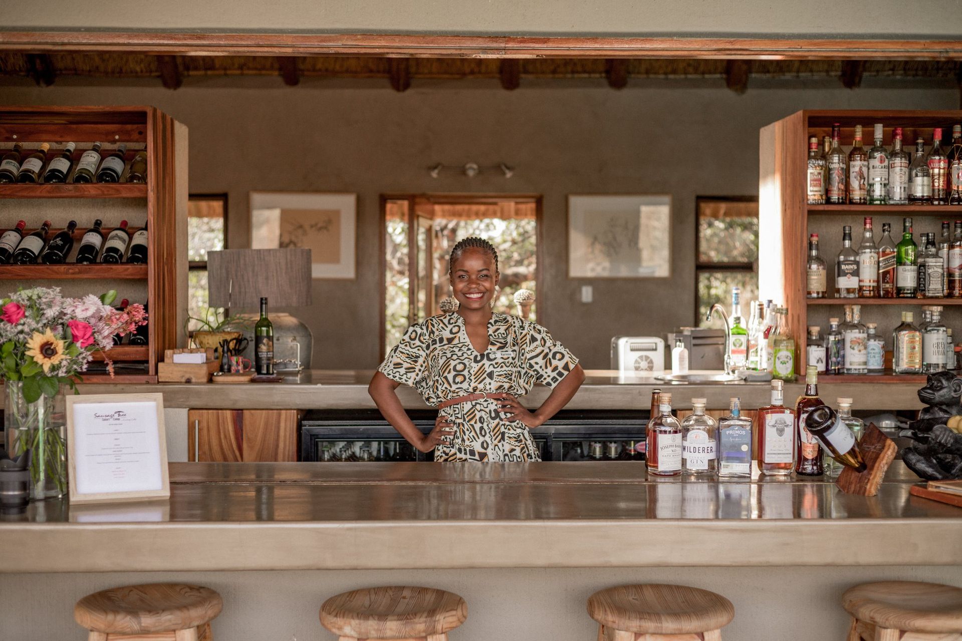 a woman stands behind a bar with bottles of alcohol including a bottle of jameson