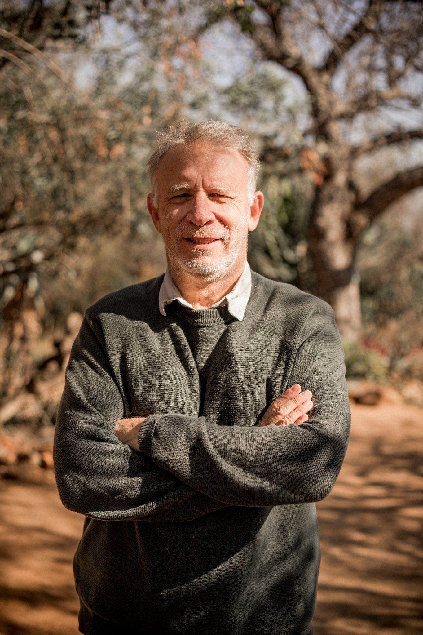 a man with his arms crossed stands in front of a tree