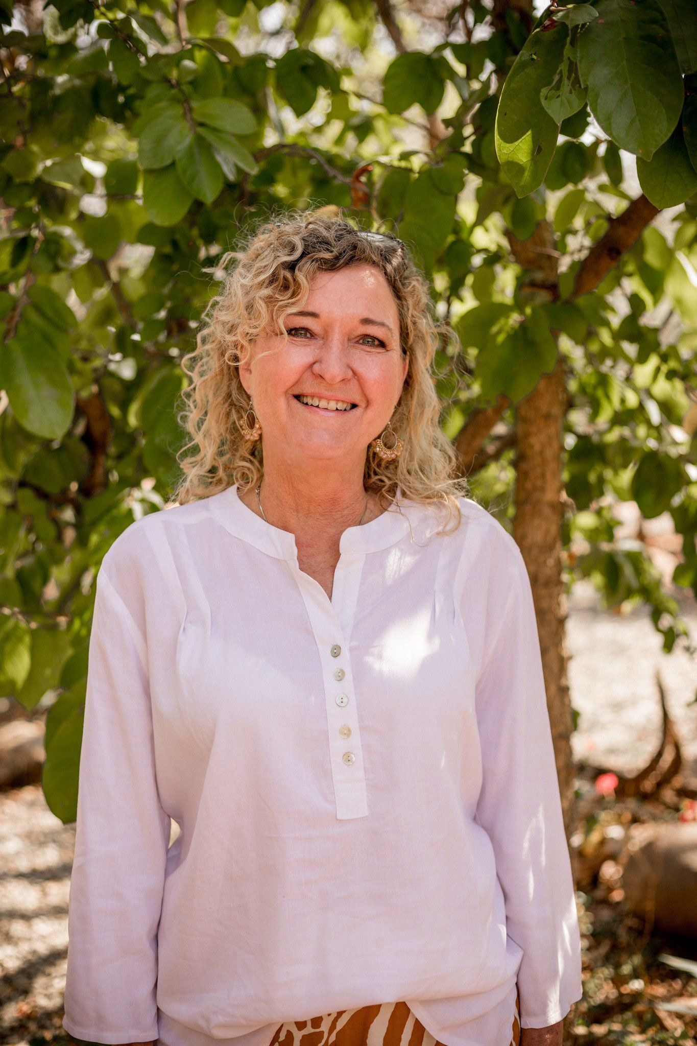 a woman in a white shirt smiles in front of a tree