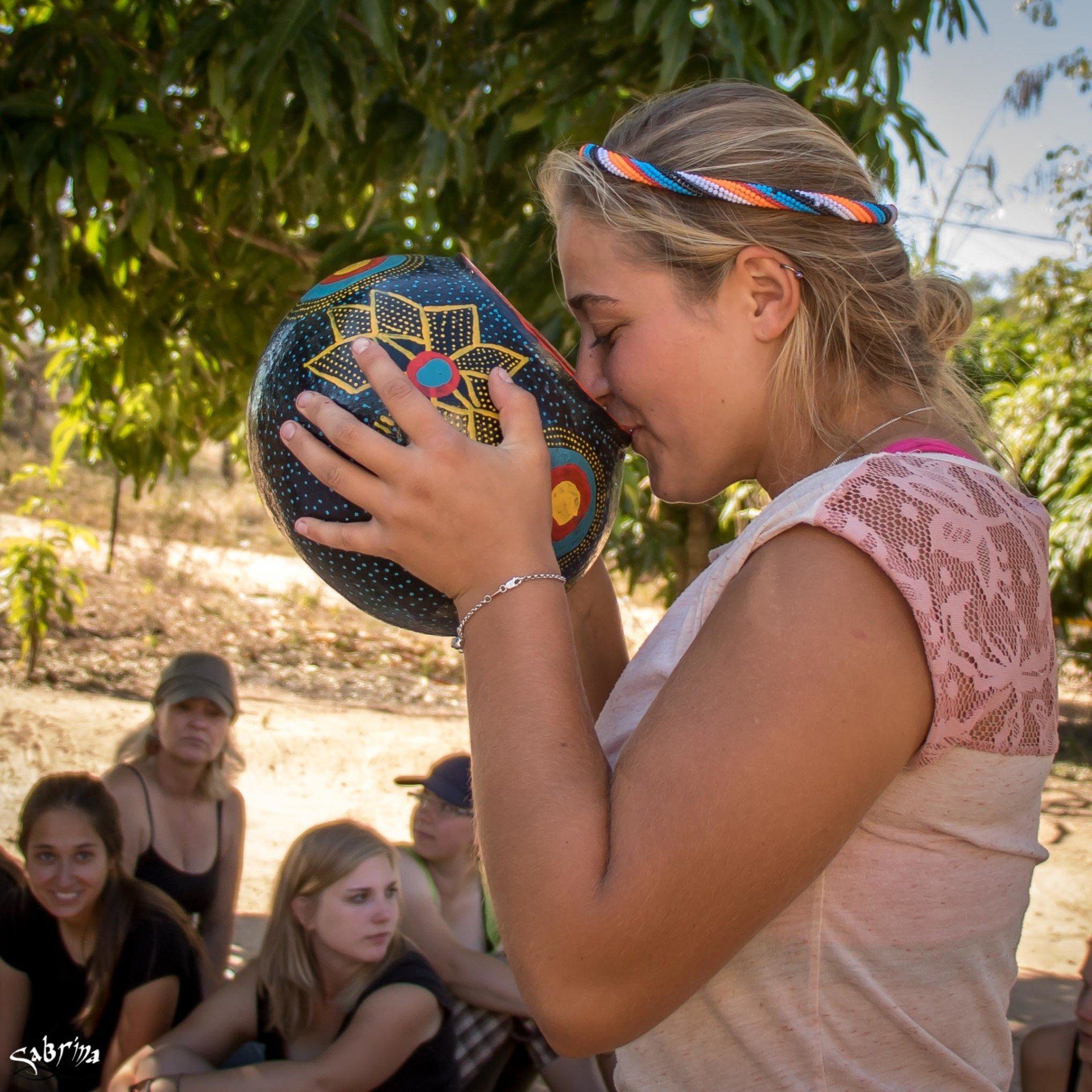 A woman is drinking from a bowl while a group of women sit behind her