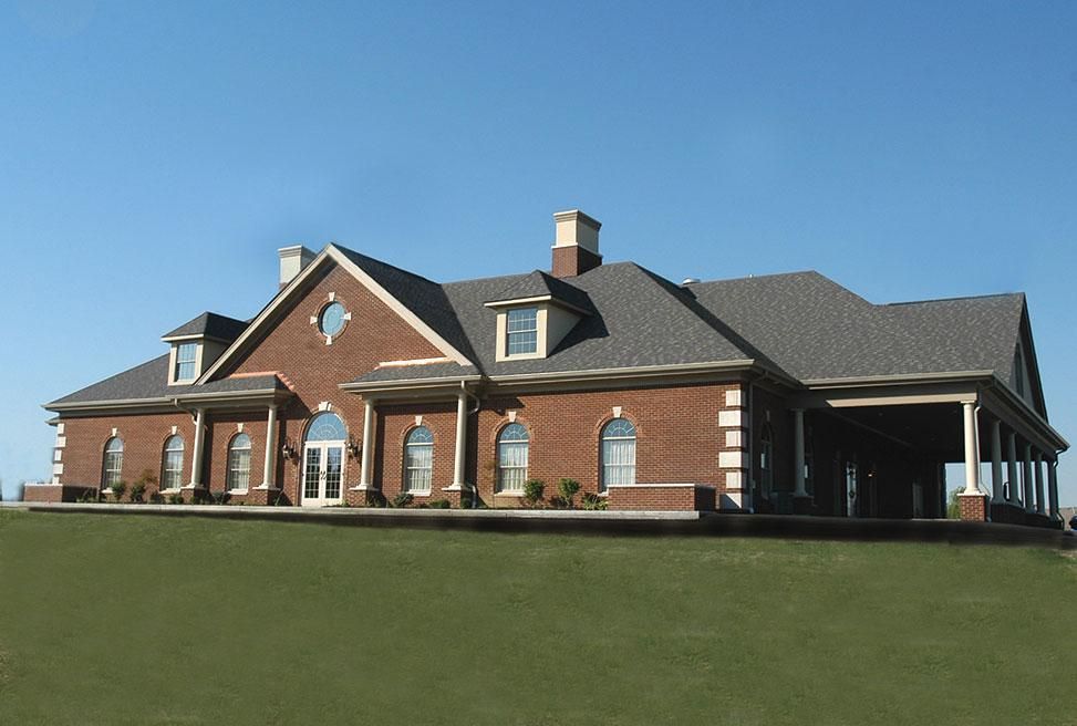 Brick suburban house with dark roof and large green lawn under a clear blue sky