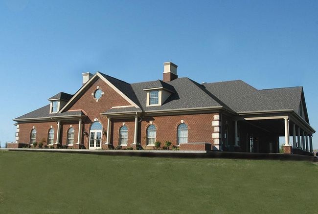 Brick suburban house with dark roof and large green lawn under a clear blue sky