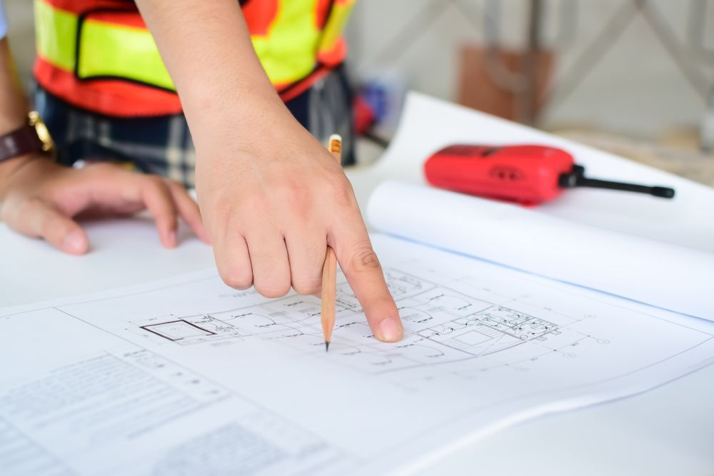 A person is pointing at a blueprint with a pencil.