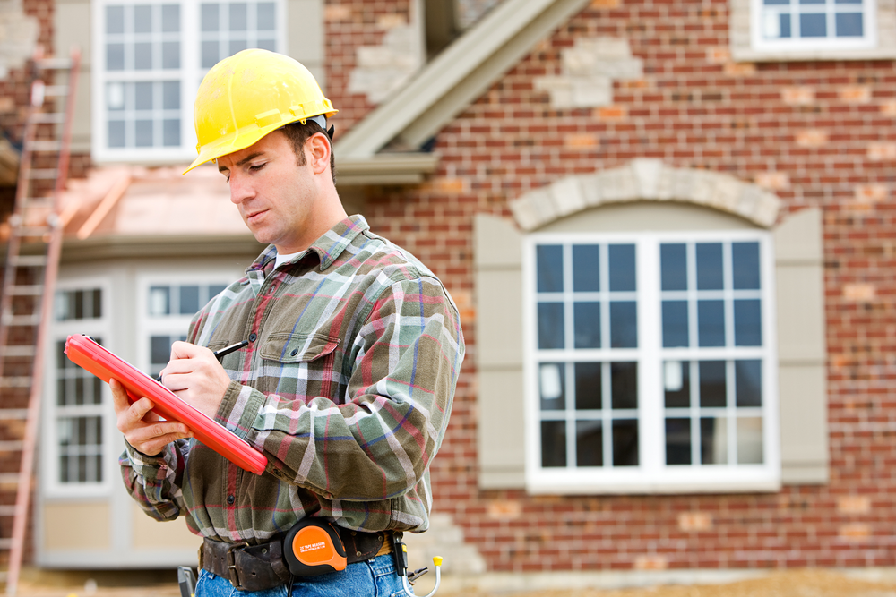 A construction worker is looking at a clipboard in front of a brick building.