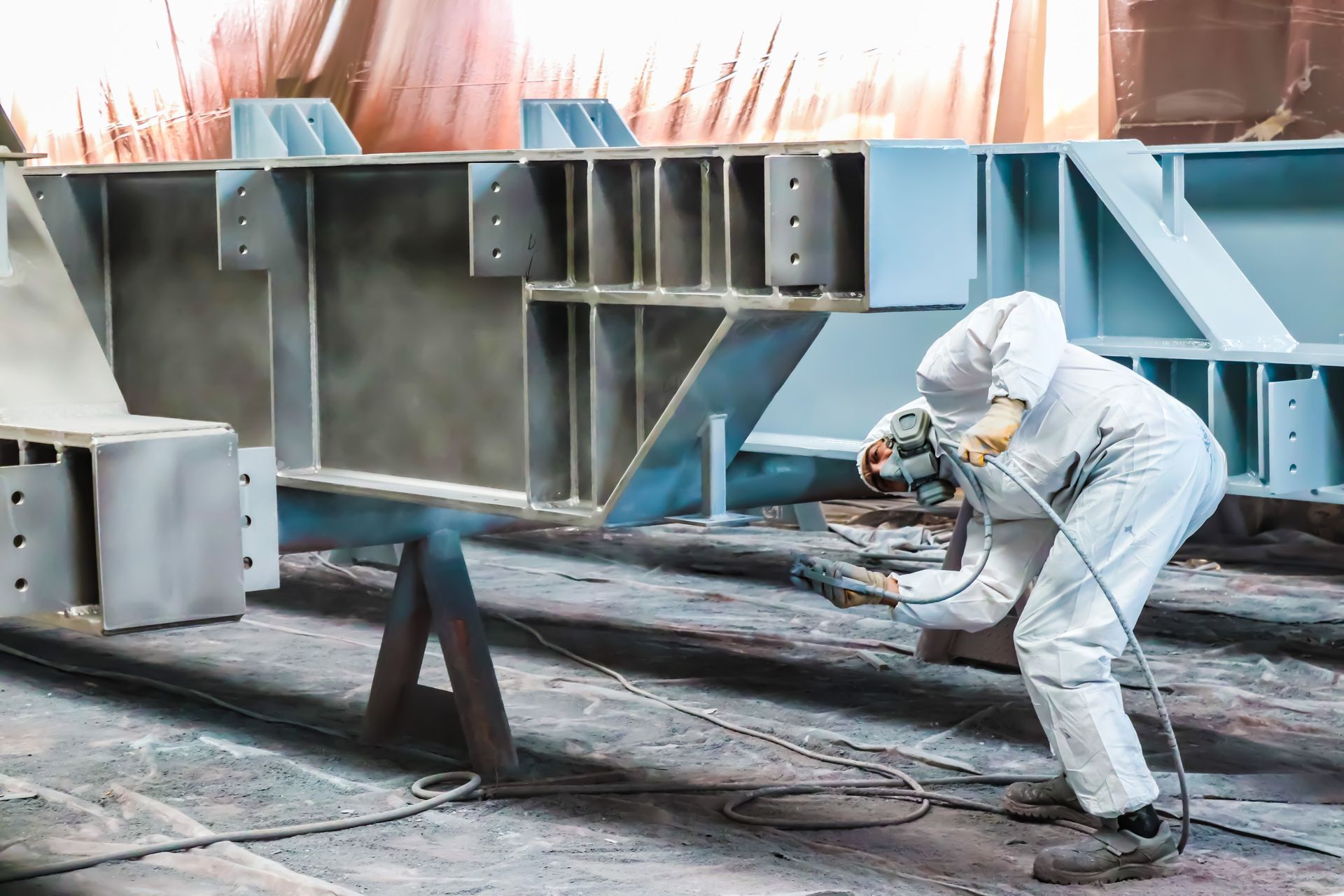 A man wearing a gas mask is spray painting a piece of metal